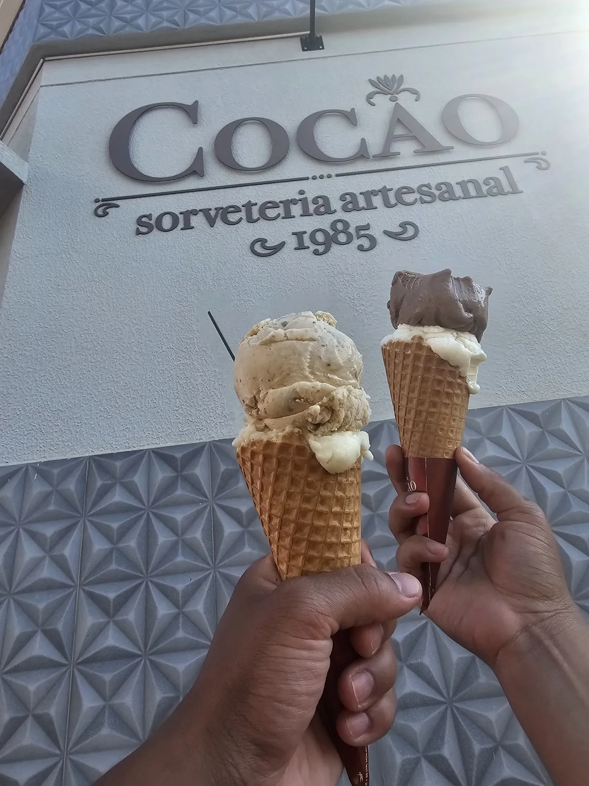 Duas casquinhas da Cocão em frente à parede com o letreiro Cocão sorveteria artesanal 1985